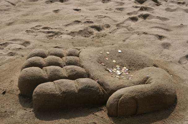 Bonus Incentive Plan Image Shows Hand Built of Sand on Beach with Coins in it