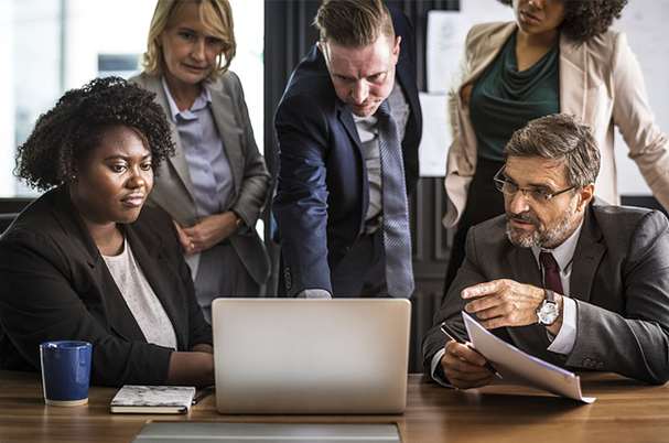 Business continuity instructions with employees gathered around a laptop in the conference room for planning