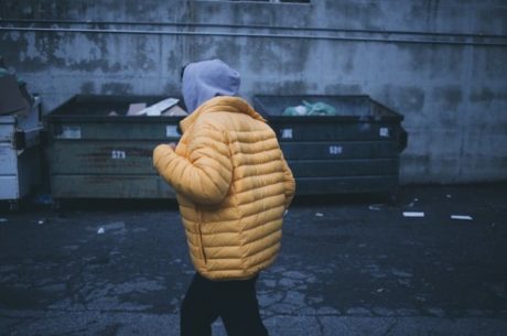 Dumpster diving shows young man walking in alley by dumpsters.