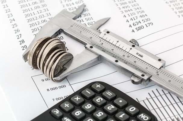 Does delaying retirement make sense with measurement gadget holding stack of coins next to calculator on financial printout.