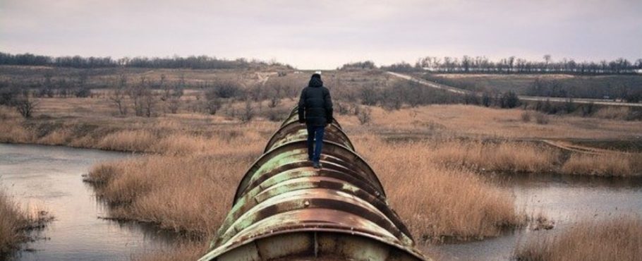 Energy photo of man in coat walking on pipeline across a field.