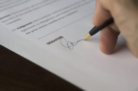 Insurance Underwriting Procedures Pen and Hand Making Signature on Insurance Document.