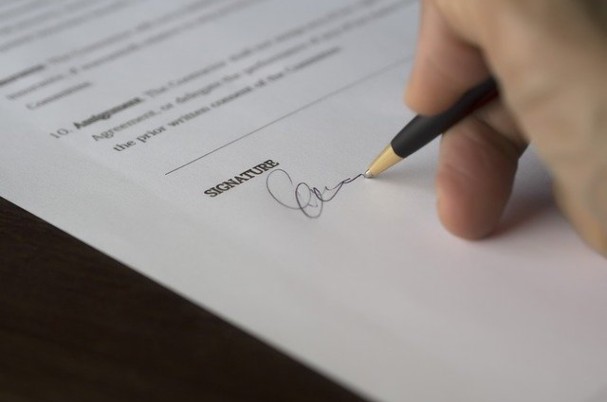 Insurance Underwriting Procedures Pen and Hand Making Signature on Insurance Document.