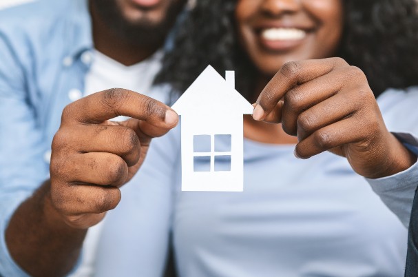 Starter Guide to Selling Your House Depicts Man and Woman Holding Paper Cutout House.