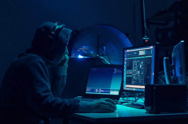 What Happens to Our Stolen Information After a Cyber Breach Image Shows Man in Hoodie Looking at a Computer.?