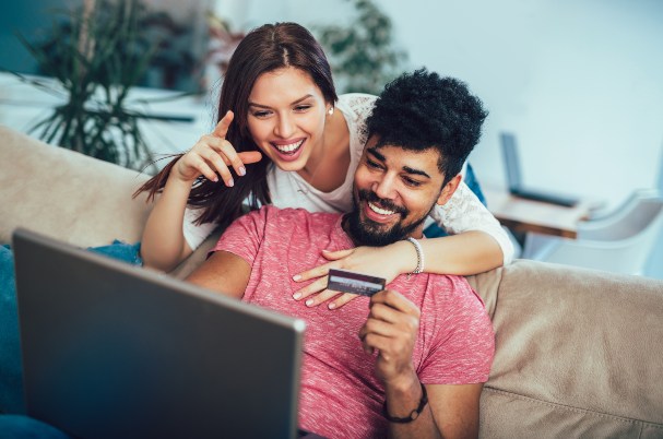 Tips for Safe Online Shopping Shows a Young Man and Woman Looking at Laptop as the Man Holds a Credit Card.