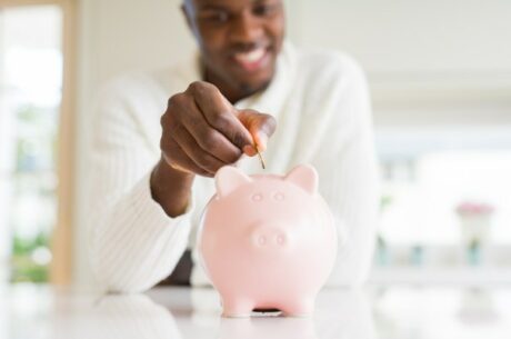 10 Reasons to Save for Retirement Shows Young Adult Man Dropping Coins in a Piggy Bank.