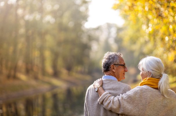 The Transition into Retirement with elderly man and woman leisurely walking along river.
