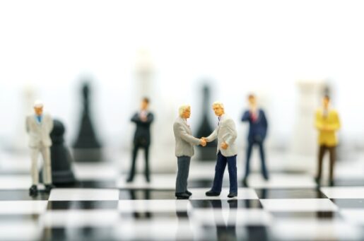 Advantages of Business Transfers photo of businessmen shaking hands while standing on a chess board.