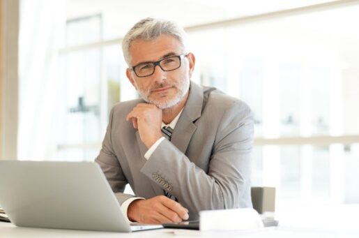 Selling your financial practice with mature financial advisor sitting at desk looking at camera