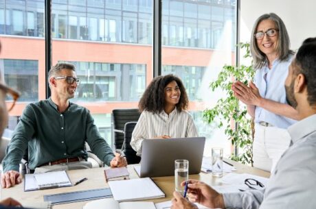 Senior older female executive CEO and happy multicultural business people discuss private foundation at boardroom table.