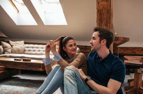 6 Money Conversations to Have in a Long-Term Relationship depicts a attractive young couple talking in the living room
