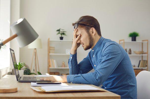 Avoiding Common 401(k) Mistakes photo concept of man with face in his hand while sitting at desk.