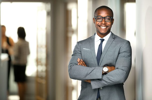 Executive's Guide to Retirement photo concept with confident businessman crossing his arms while standing in front of an office entrance.