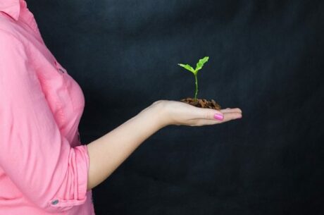 Introduction to 403(b) Plans photo concept with woman in pink blouse holding a sprouting plant in front of a dark background.