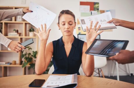 Active vs. Passive Portfolio Management with business woman holding hands up and closing eyes, with obvious frustration at people pushing financial data at her. on laptop, tablet, notes, and reports.