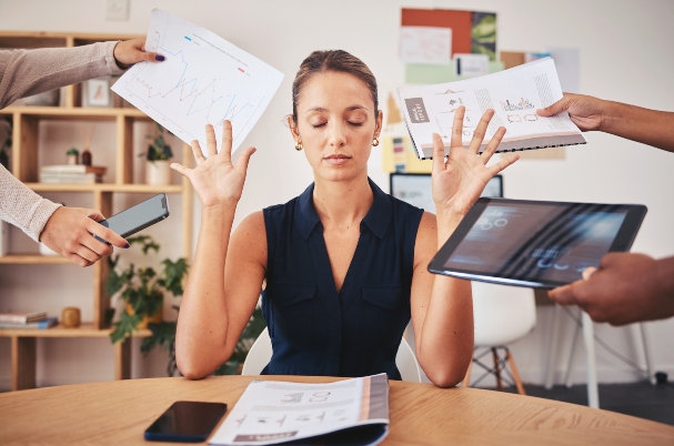 Active vs. Passive Portfolio Management with business woman holding hands up and closing eyes, with obvious frustration at people pushing financial data at her. on laptop, tablet, notes, and reports.