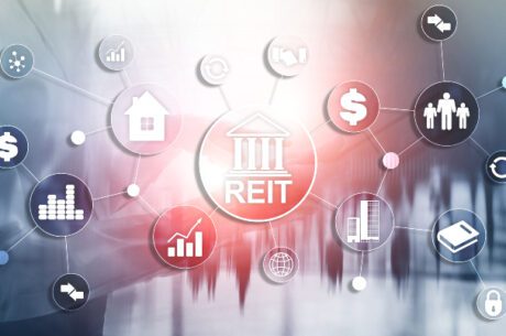 REITs Unveiled: A Comprehensive Guide for Investors is depicted in the image by REIT graphic in the middle of several floating related graphics of buildings, graphs, and dollar signs.