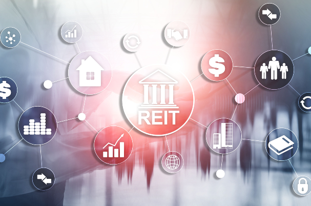 REITs Unveiled: A Comprehensive Guide for Investors is depicted in the image by REIT graphic in the middle of several floating related graphics of buildings, graphs, and dollar signs.